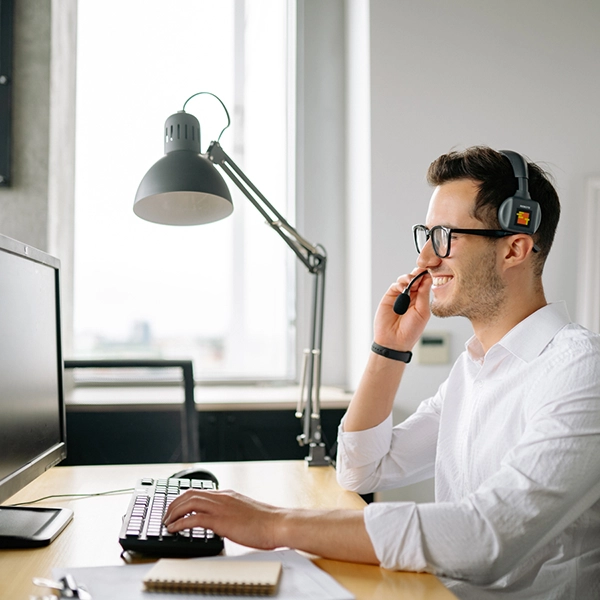smiling customer support specialist speaking on headset in front of computer